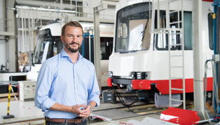 Samuel Kermelk steht vor Straßenbahnen in einer Produktionshalle