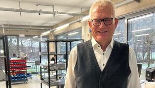 Jens Trepte steht in einer Produktionshalle mit großen Fenstern vor Regalen